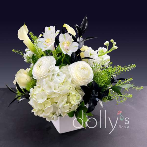 White floral arrangement in a square vase with calla lilies and hydrangeas