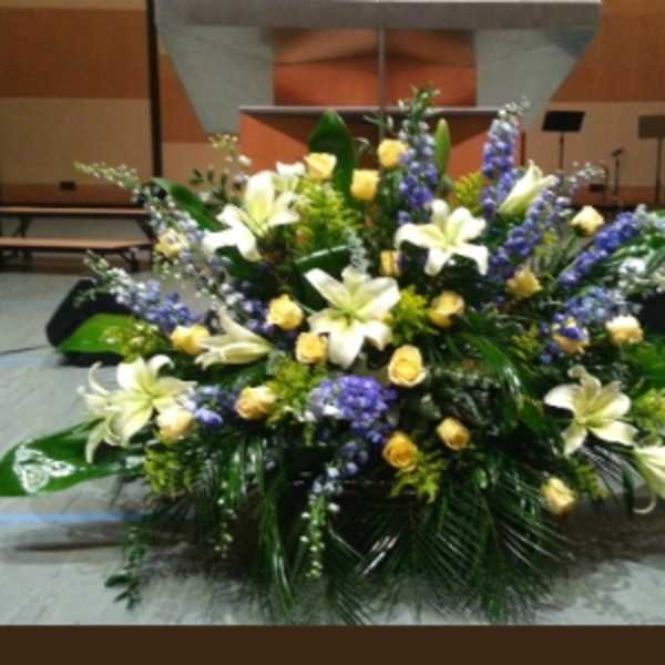 Large altar arrangement with white lilies, yellow roses, and purple flowers in a fan-shaped design