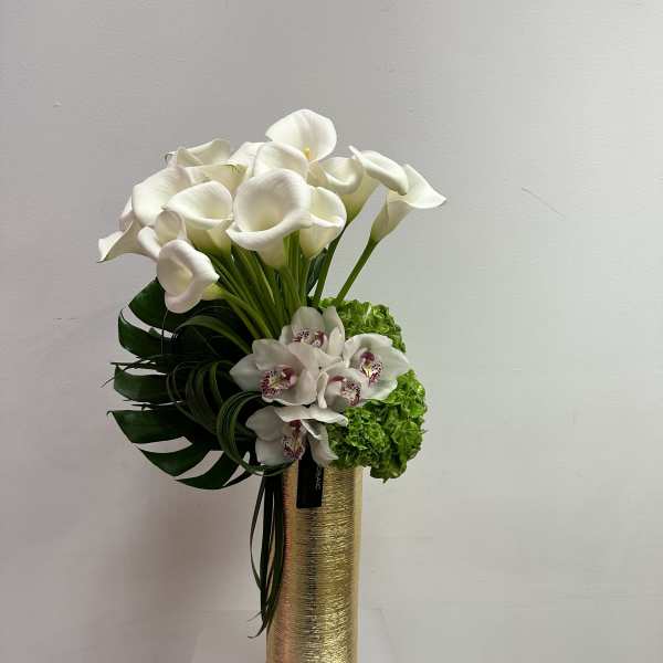 Tall gold vase with white calla lilies, green hydrangea, and white orchids in a modern arrangement
