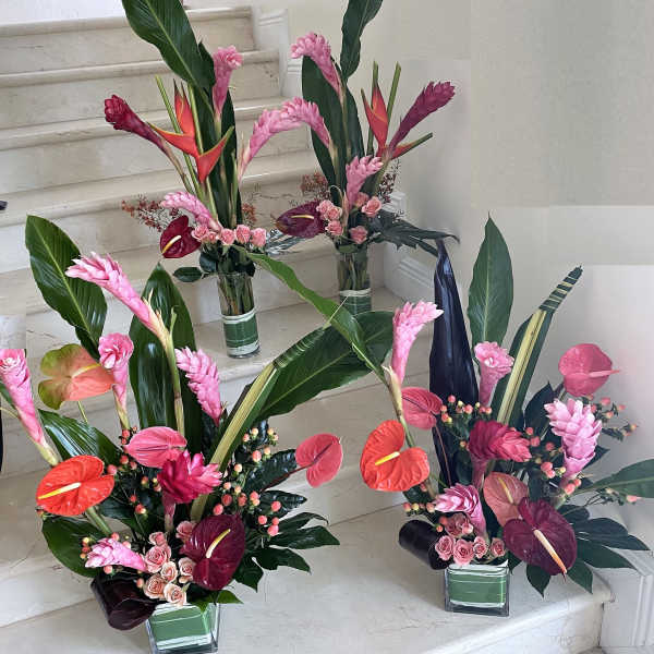 Set of three tall tropical arrangements with pink gingers, anthuriums, and roses in glass vases