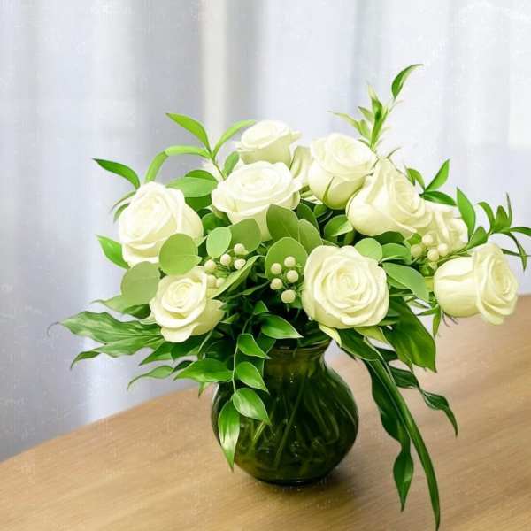 White roses arranged in a green glass vase with lush foliage