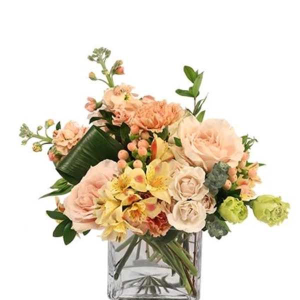 Peach and cream flower arrangement in a clear square vase