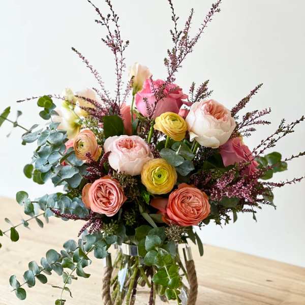 Mixed pink and peach flowers in a glass vase with eucalyptus