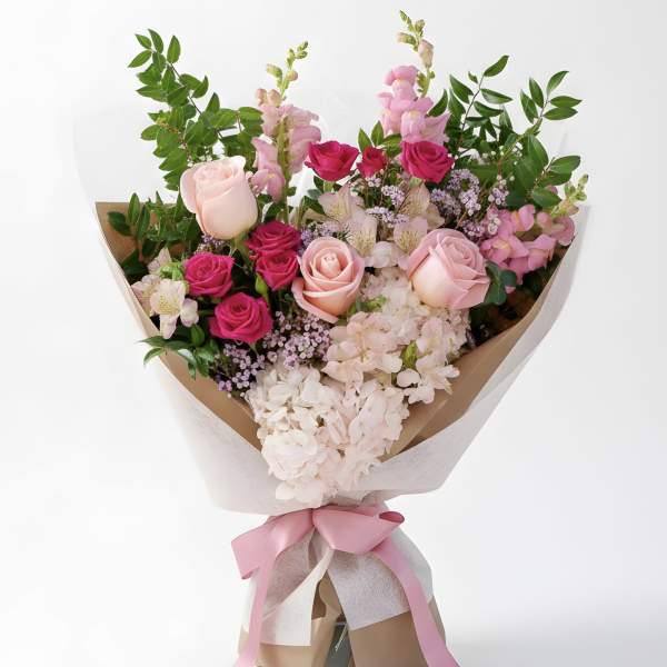 Bouquet of pink roses and pale hydrangeas with greenery, wrapped in paper and tied with a pink ribbon.