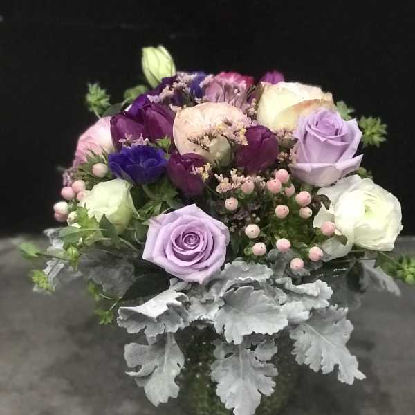 Bouquet of purple, pink, and white roses with silver foliage in a vase