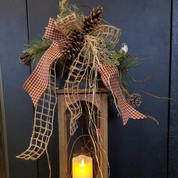 Rustic wooden lantern with glowing candle, pinecones, and plaid ribbon accents