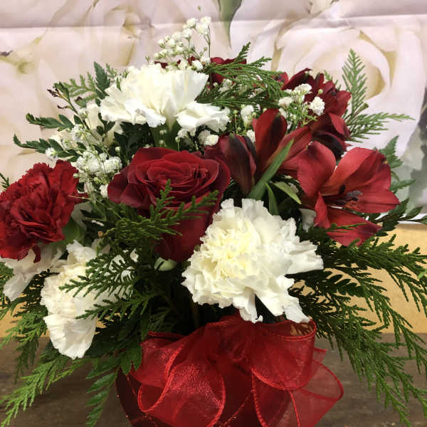 Red and white floral arrangement in a red vase with a ribbon