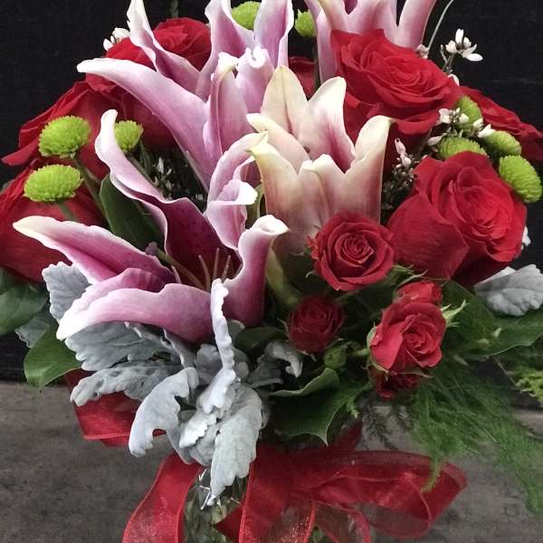 Red roses and pink lilies in a glass vase with a red ribbon