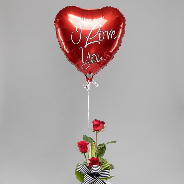 Red heart I Love You balloon with three red roses in a red vase and a white teddy bear.