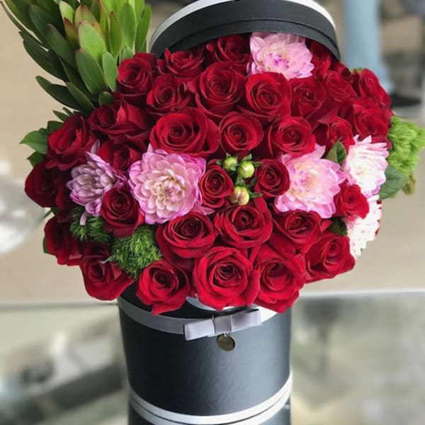 Red roses and pink flowers arranged in a black hat box