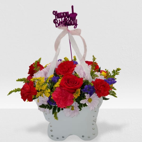 Basket arrangement of red roses, carnations, and mixed blooms with a Happy Birthday pick.