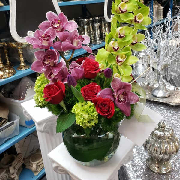 Arrangement of pink and green orchids with red roses in a glass vase