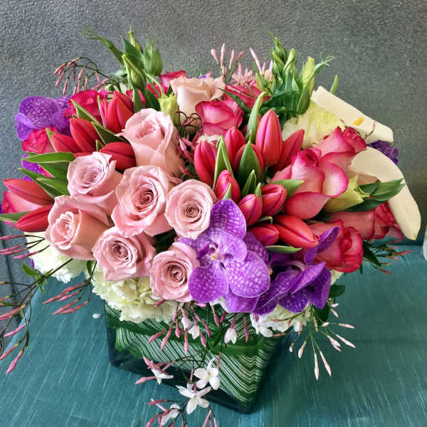 Bouquet of pink roses, red tulips, and purple orchids in a glass vase
