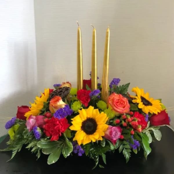 Floral centerpiece with three gold taper candles and bright mixed blooms