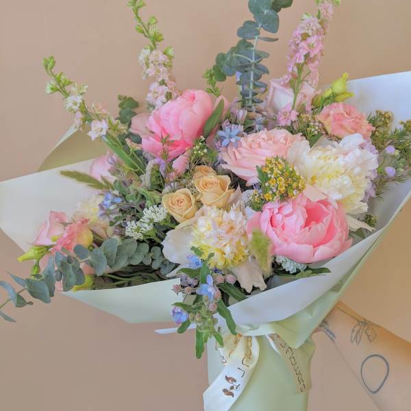 Pastel bouquet of pink, peach, and white flowers wrapped in pale paper