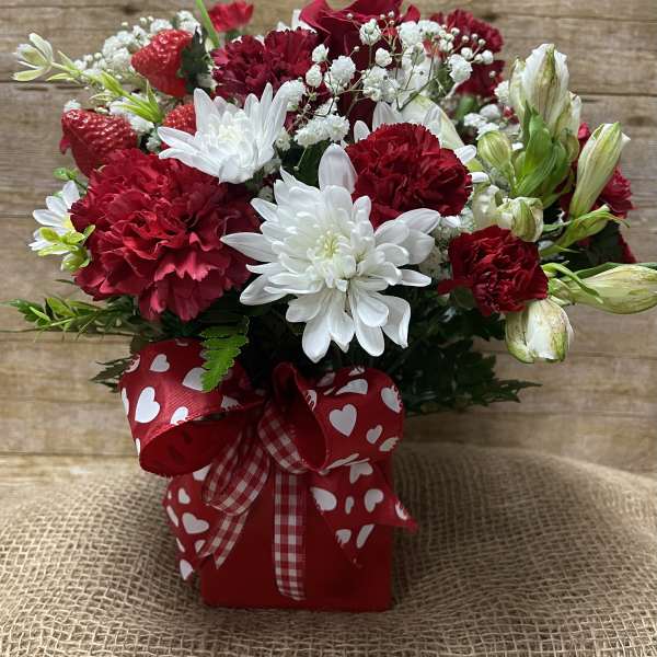 Red and white flower arrangement in a heart-patterned box with ribbon