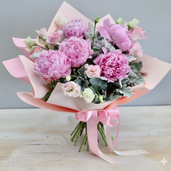 Hand-tied bouquet of pink peonies and pale lisianthus wrapped in pink paper with a satin ribbon