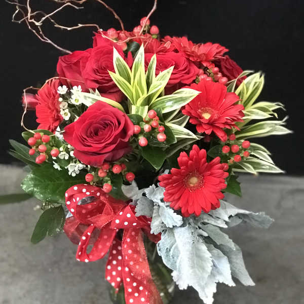 Red roses and gerbera daisies in a glass vase with a red ribbon