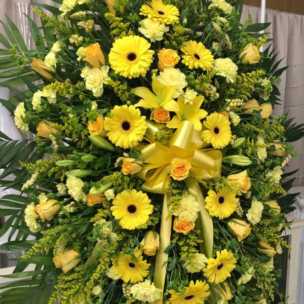 Large yellow floral standing spray with gerberas, roses, lilies, and ribbon