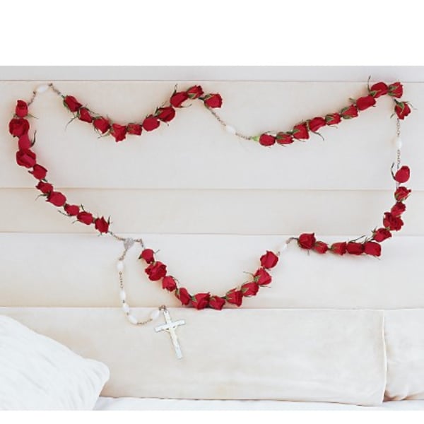 Red rose garland draped across a white upholstered headboard with a cross pendant