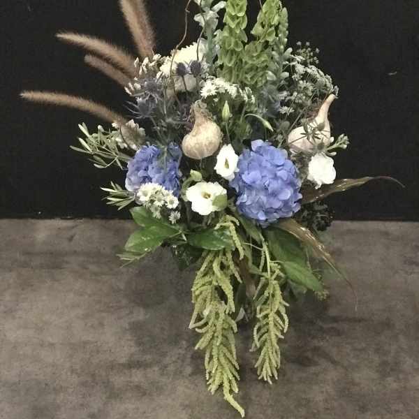 Tall floral arrangement with blue hydrangeas, white blooms, and dried grasses