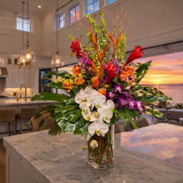 Tall tropical bouquet with white orchids and red-orange flowers in a glass vase