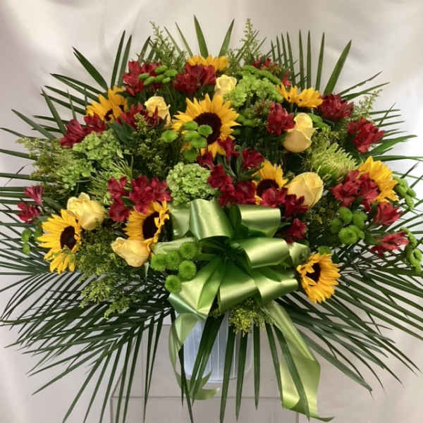 Large floral spray with sunflowers, red blooms, and a green ribbon bow