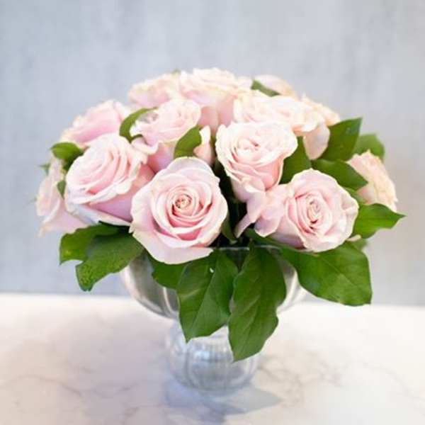 Low round arrangement of pale pink roses in a clear glass vase on a marble surface