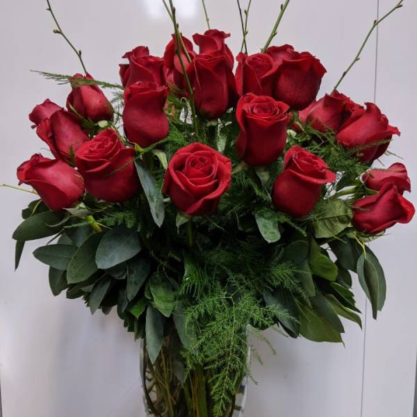 Red roses arranged in a clear glass vase with greenery