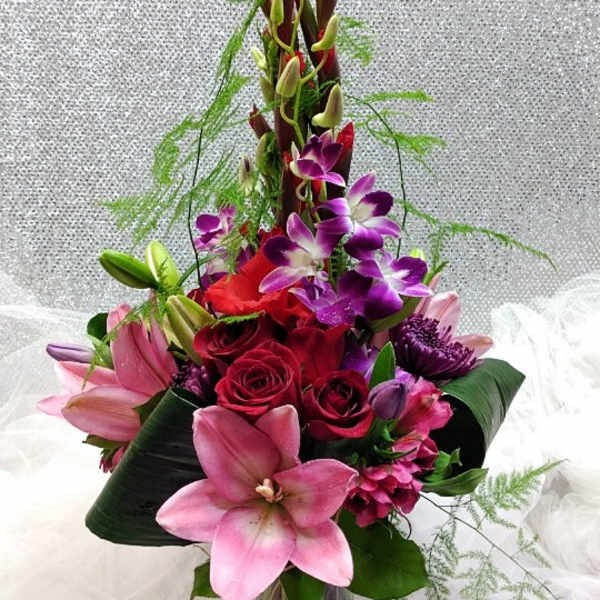 Tall bouquet of pink lilies, red roses, and purple orchids in a glass vase