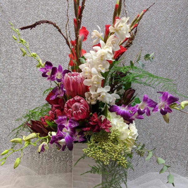 Tall floral arrangement with purple orchids, white orchids, and red tropical blooms in a white vase