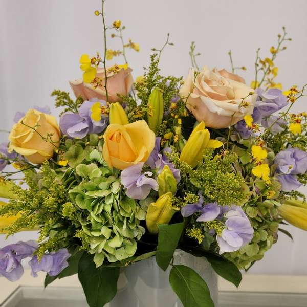 Pastel bouquet of roses, hydrangeas, and yellow orchids in a white vase