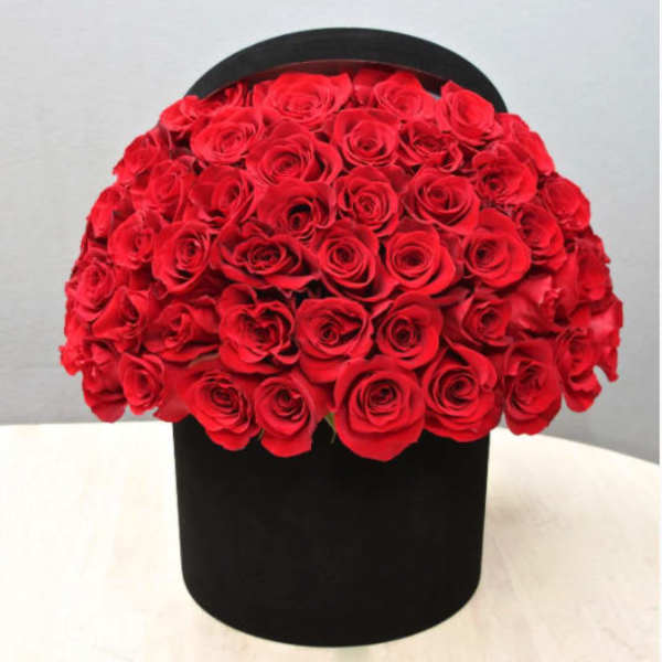 Large dome of red roses arranged in a round black hatbox-style container on a light table.