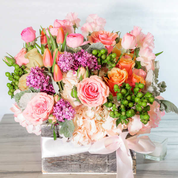 Square wooden box arrangement with pink roses, orange tulips, lilac blooms, and green berries