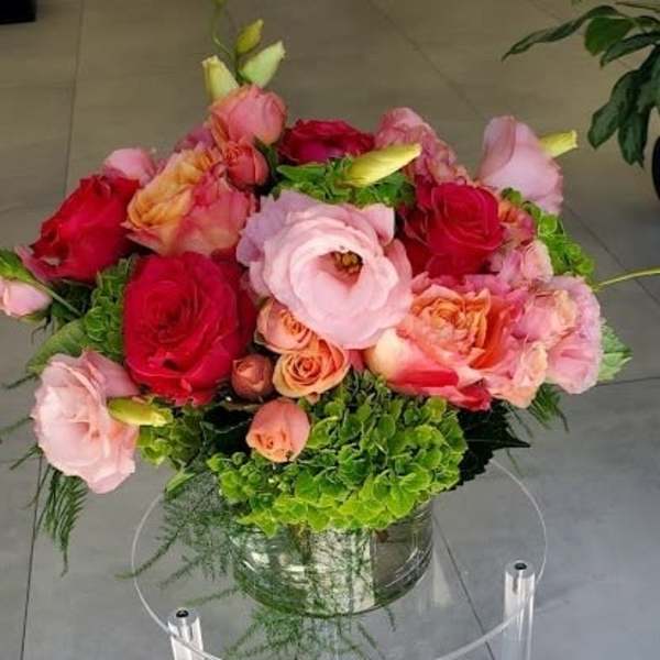 Round arrangement of pink and red roses and lisianthus with green hydrangea in a glass vase