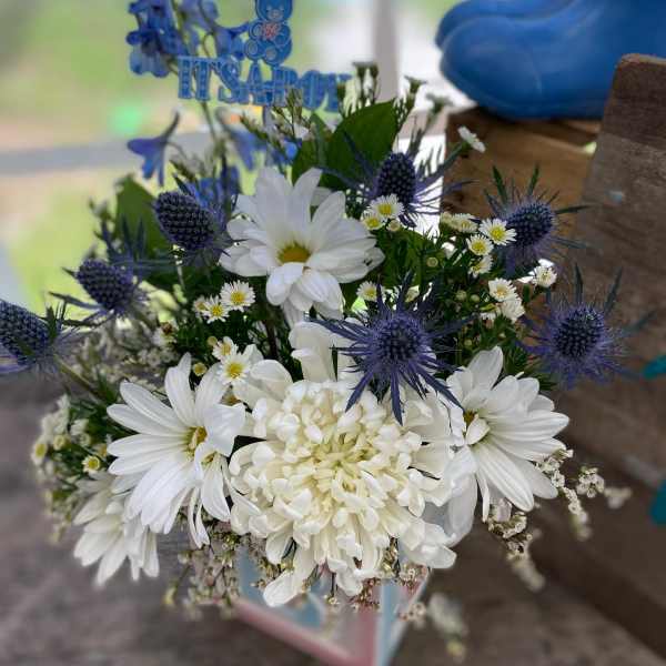 White daisies and mums with blue thistle-like blooms in a cube vase with an 'It's a Boy' pick