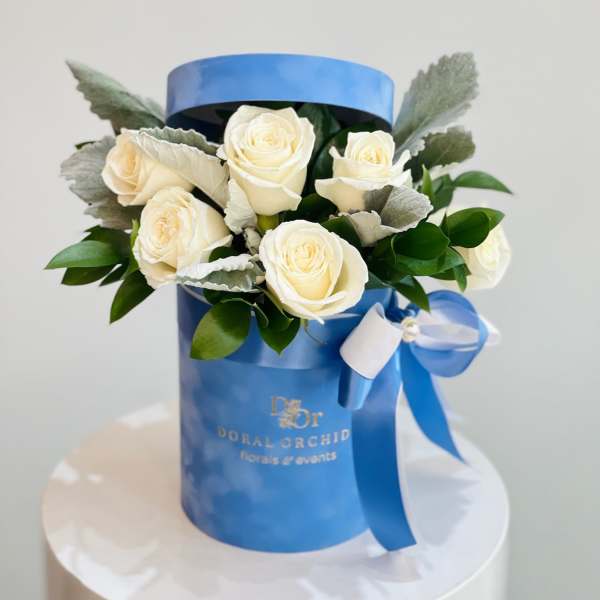 White roses arranged in a blue gift box with a ribbon