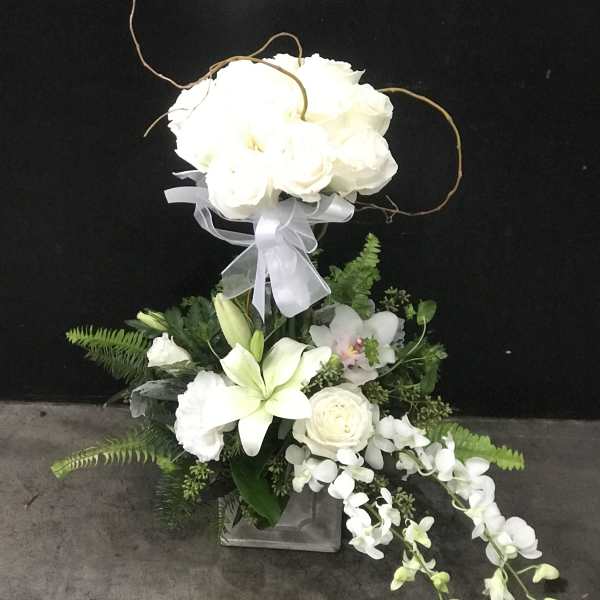 White floral arrangement with lilies, roses, and orchids in a square vase