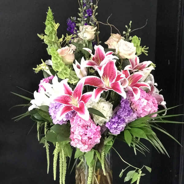 Tall bouquet of pink lilies, roses, and hydrangeas in a glass vase