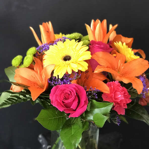 Bright mixed bouquet with orange lilies, pink roses, and yellow daisies in a glass vase