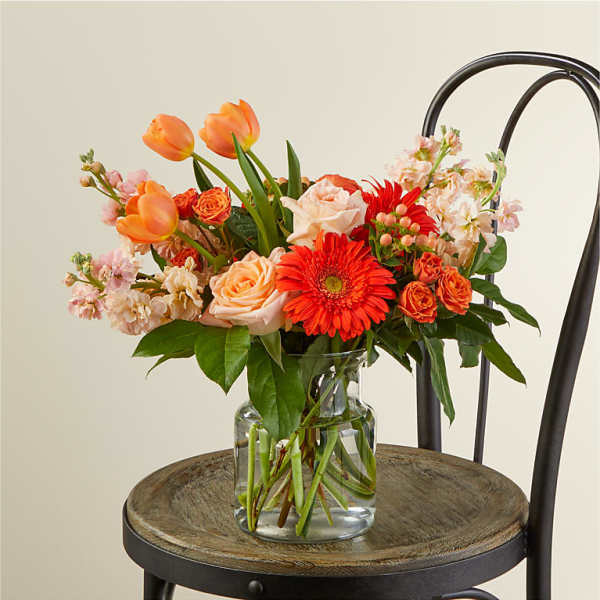 Mixed bouquet of orange and peach flowers in a clear glass vase
