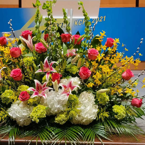 Large stage floral arrangement with pink roses, stargazer lilies, white hydrangeas and yellow flowers