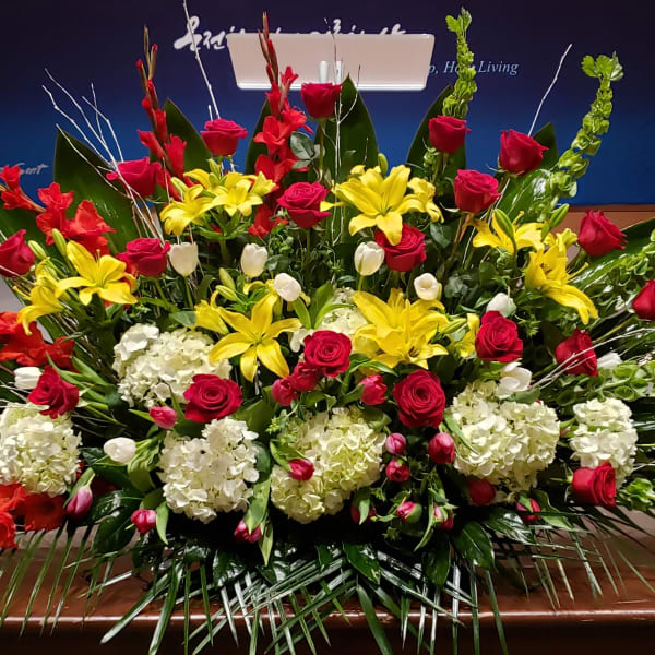 Large altar-style arrangement of red roses, yellow lilies, white hydrangeas, and tulips in a fan shape