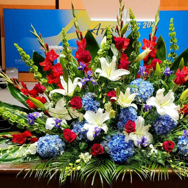 Large red, white, and blue stage floral spray with lilies, roses, gladiolus, and hydrangeas.