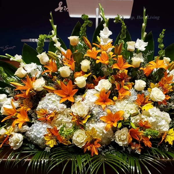 Large altar-style arrangement of orange lilies and white roses with hydrangeas in a low horizontal design
