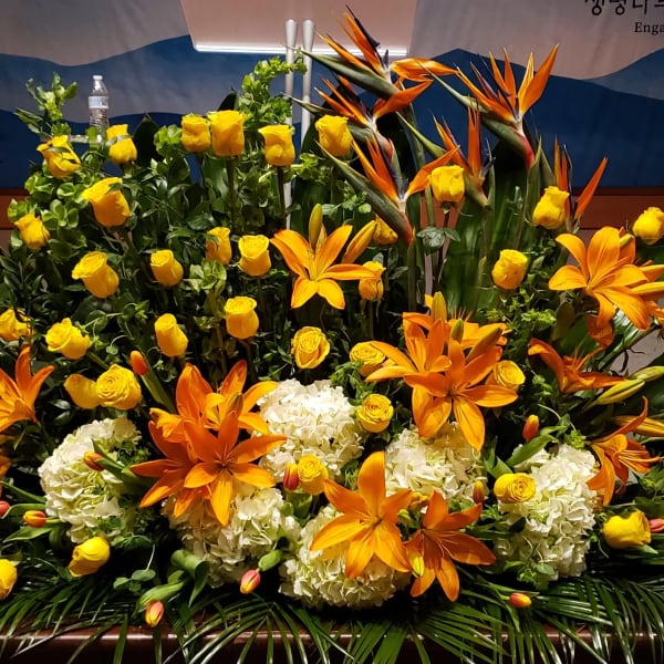Large altar arrangement of orange lilies, yellow roses, tropical blooms and white hydrangeas.
