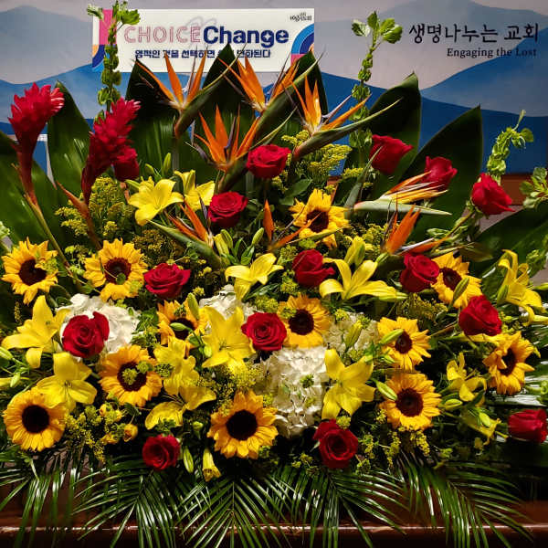 Large altar arrangement with yellow lilies, sunflowers, red roses and tropical flowers in a fan shape
