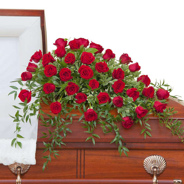 Red rose casket spray arranged across a polished wooden casket.