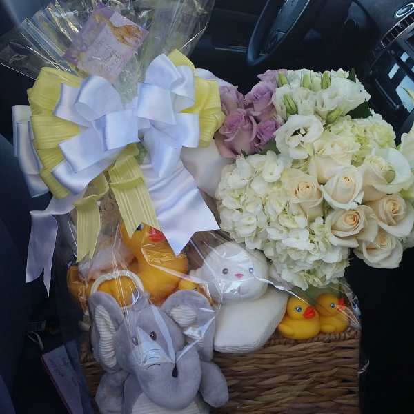 Basket of white and lavender flowers with plush toys and ribbon bows