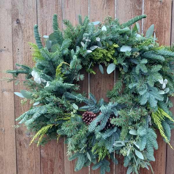 Evergreen wreath with pinecones and mixed foliage hanging on a wooden fence